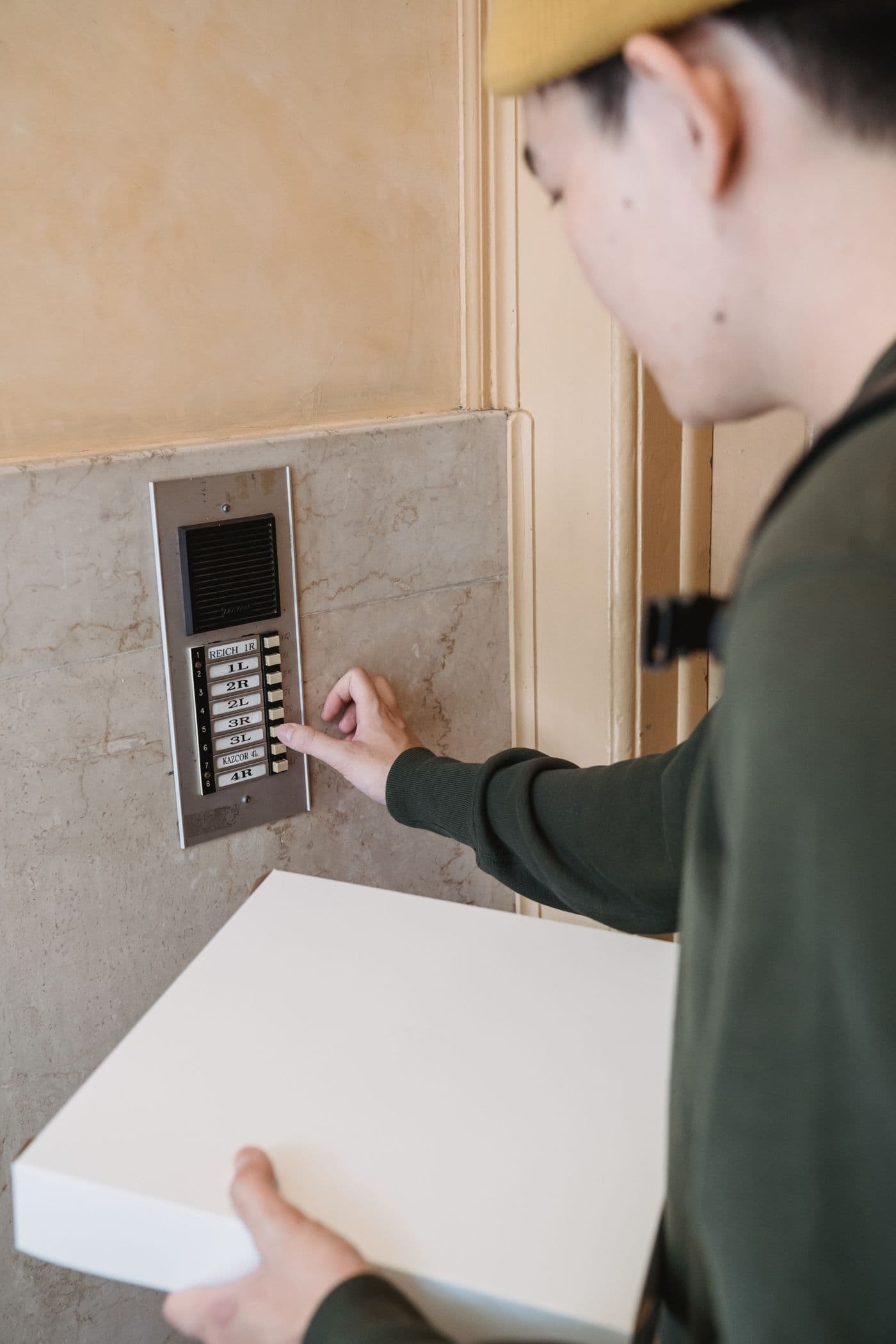 Personne sonnant à un interphone d'immeuble avec un colis